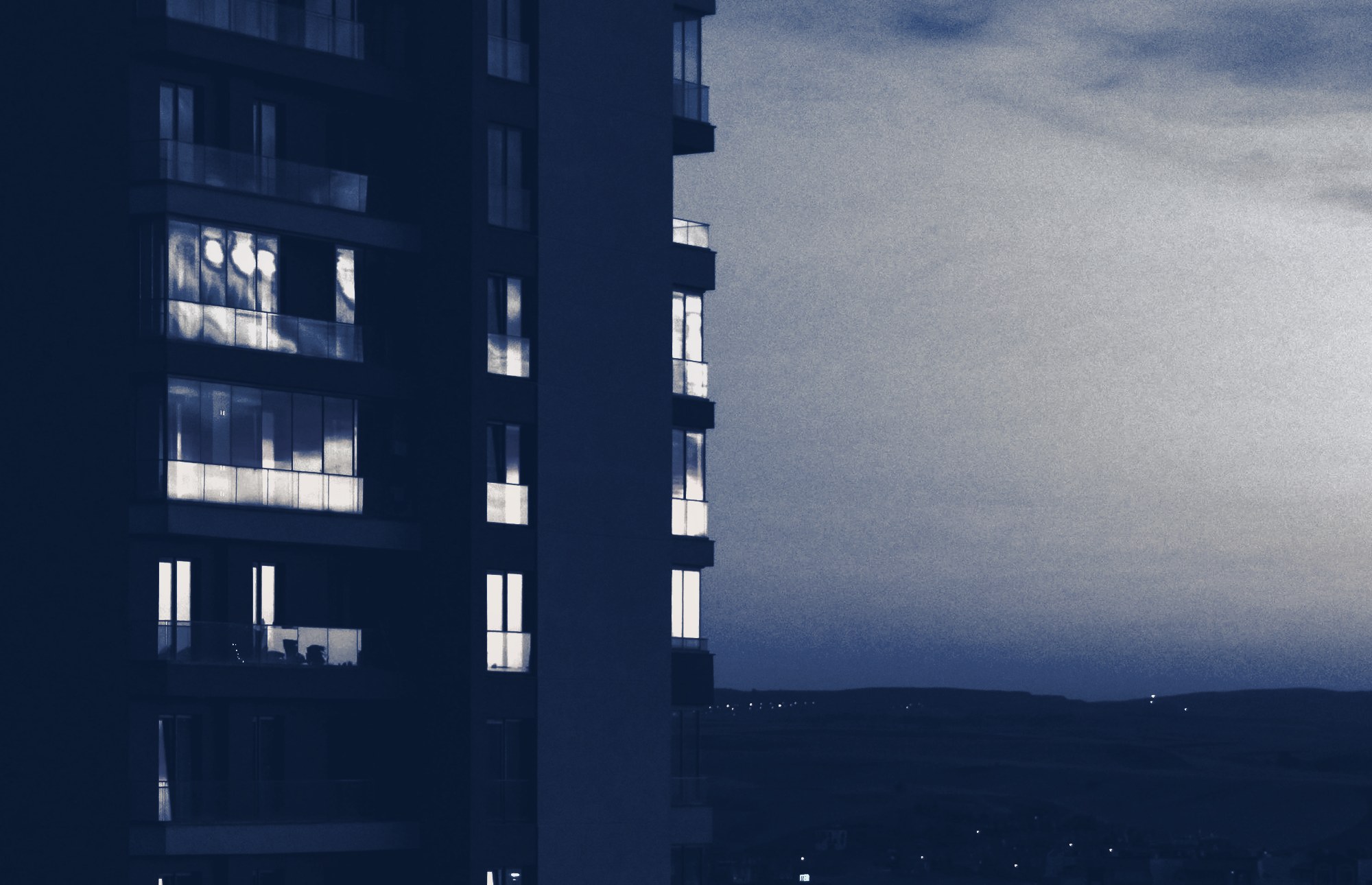 Modern residential tower at dusk with lit windows, tinted navy