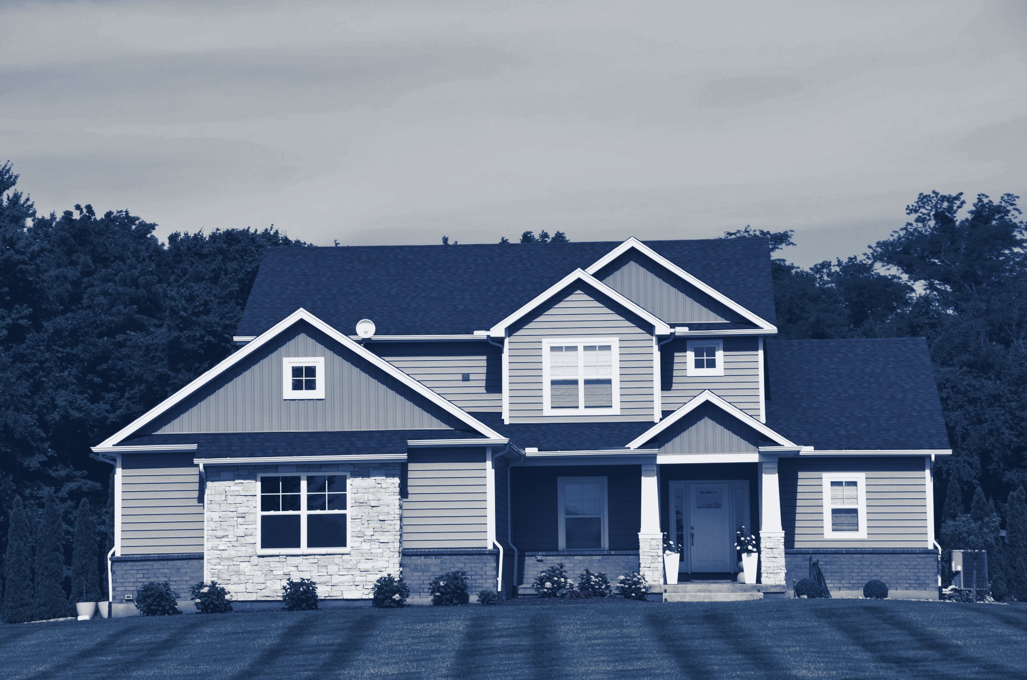 Well-kept two-story grey house with striped green lawn, shrubs and trees, tinted navy