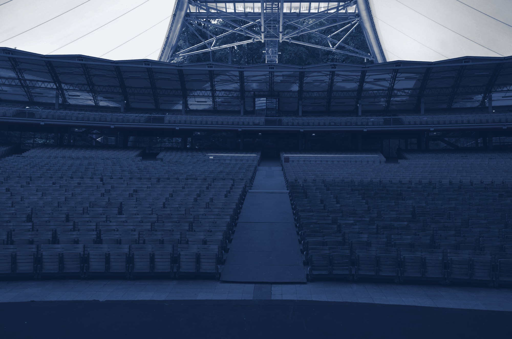 Empty open-air amphitheater: rows of seats split by a wide central aisle leading to rear exits under a canopy, tinted navy